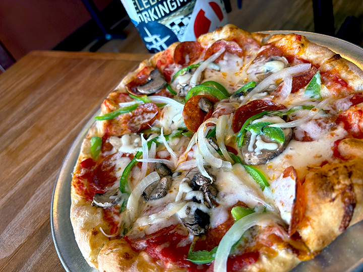 Close-up of a pizza with pepperoni, green peppers, onions, mushrooms, and melted cheese on a silver tray.