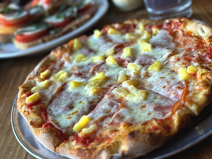 A pizza with melted cheese, ham, and pineapple slices on a pizza crust.