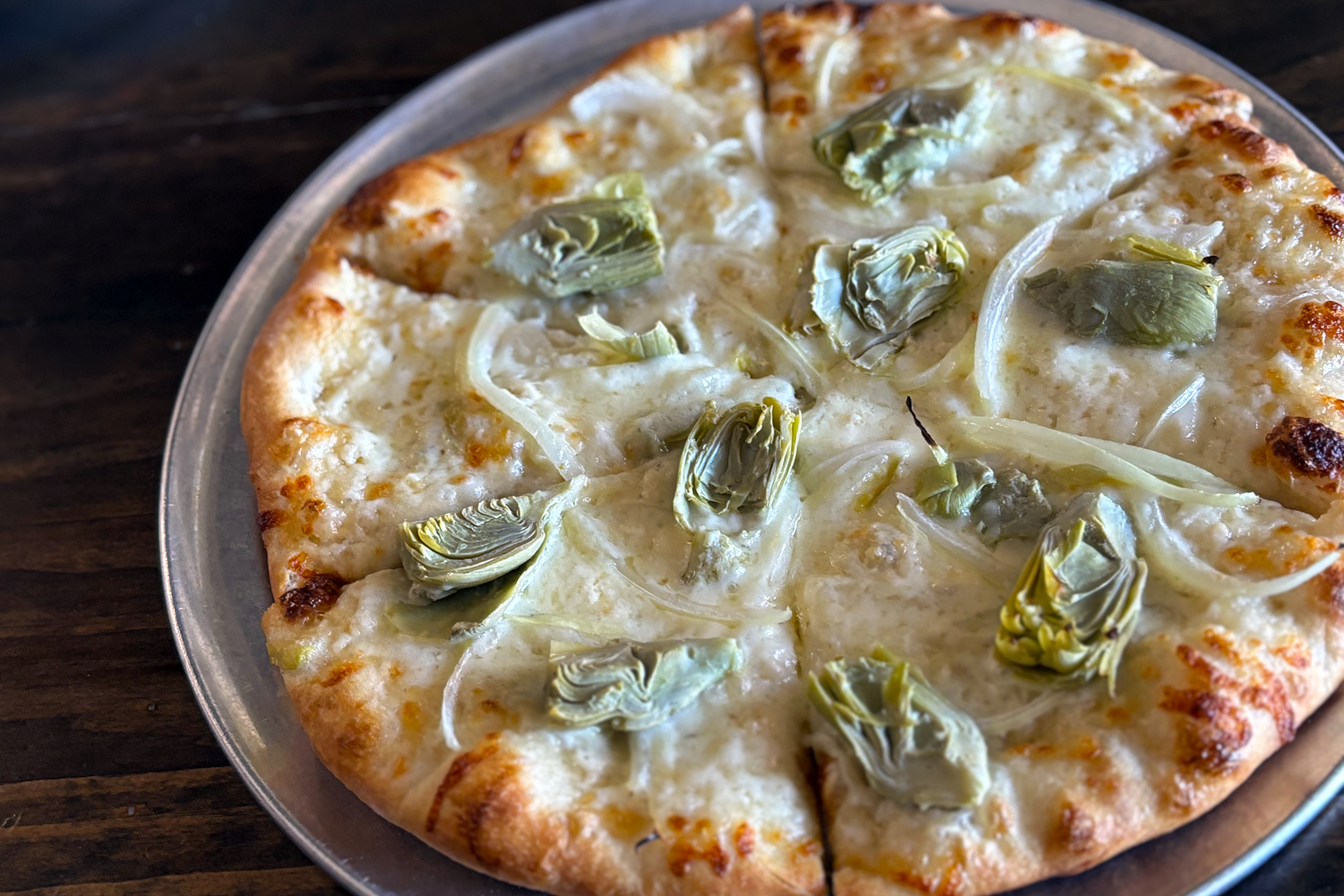 Cheese and artichoke pizza on a metal tray with a dark wooden background.