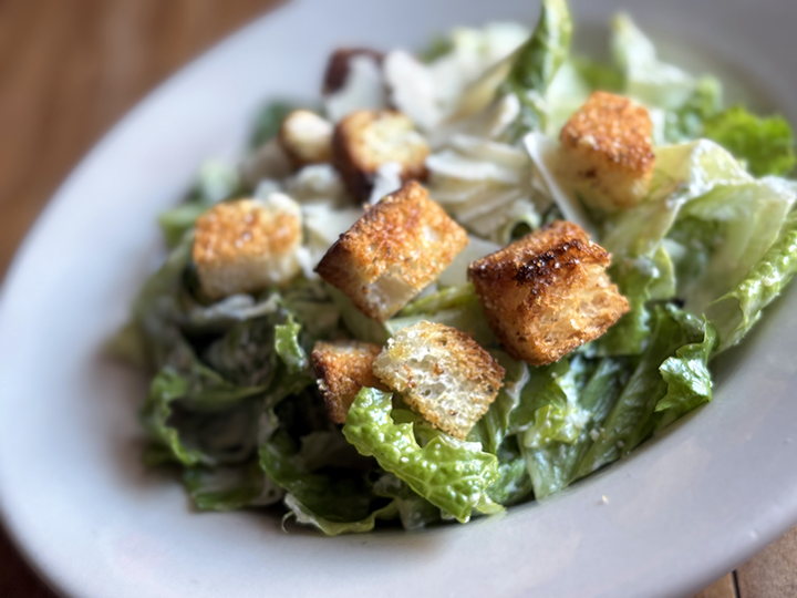 A Caesar salad with chopped romaine lettuce, croutons, and grated cheese on a white plate.