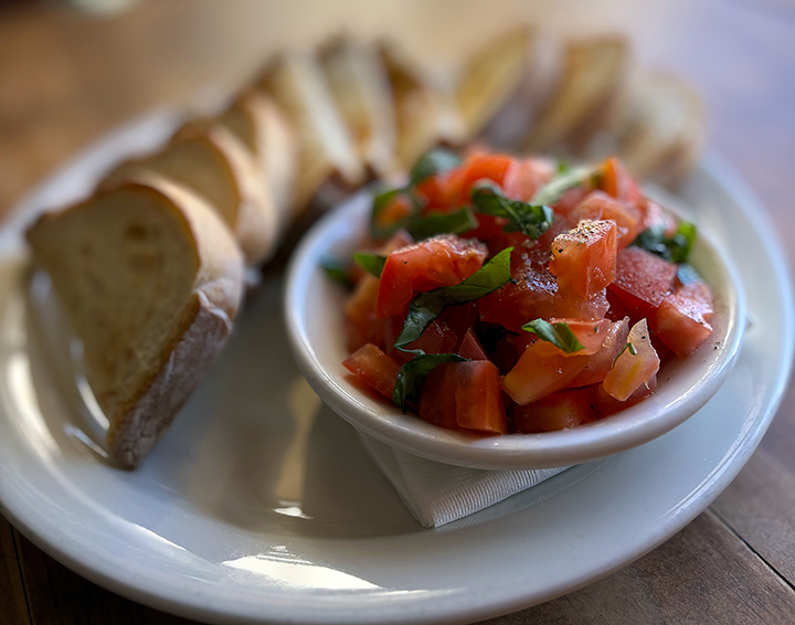 Sliced baguette bread with a bowl of chopped tomato and basil salsa on a white plate.