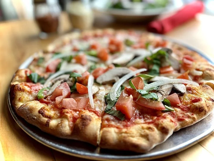 Freshly baked pizza with tomato, basil, and onion toppings on a black plate.