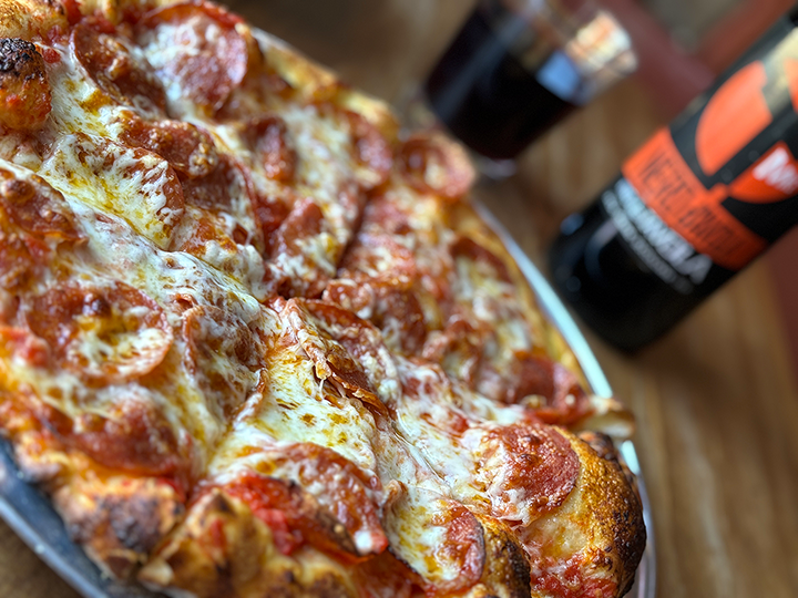 Close-up of a pepperoni pizza with melted cheese on a wooden table, with a bottle of soda in the background.