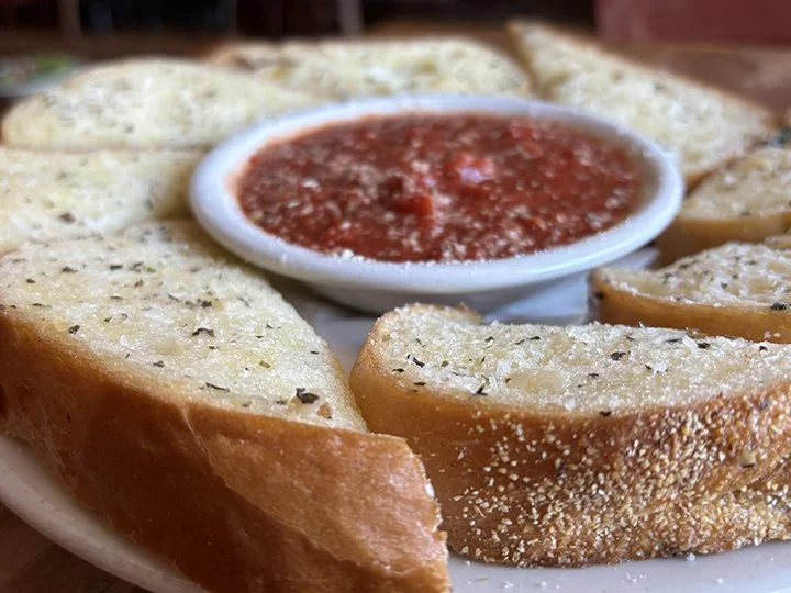 Slices of garlic bread arranged around a bowl of marinara sauce.
