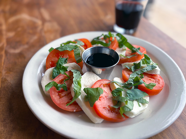 Caprese salad with sliced tomatoes, mozzarella cheese, fresh basil, and balsamic glaze on a white plate.