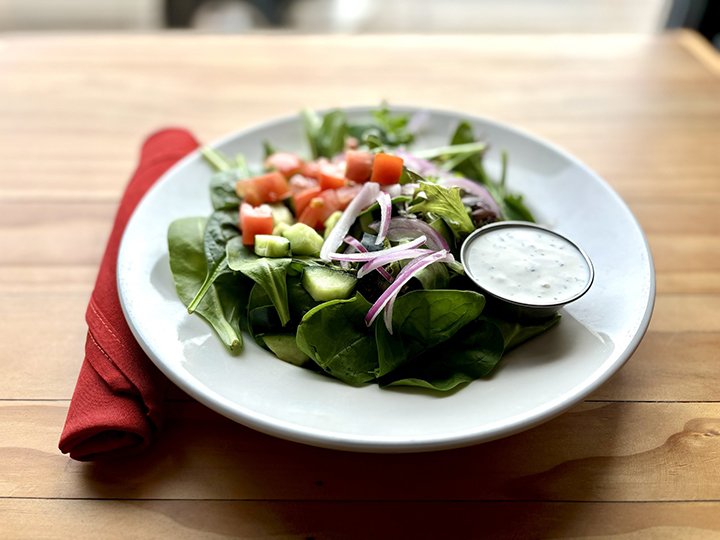 Fresh garden salad with spinach, diced carrots, chopped celery, sliced red onions, with a side of ranch dressing