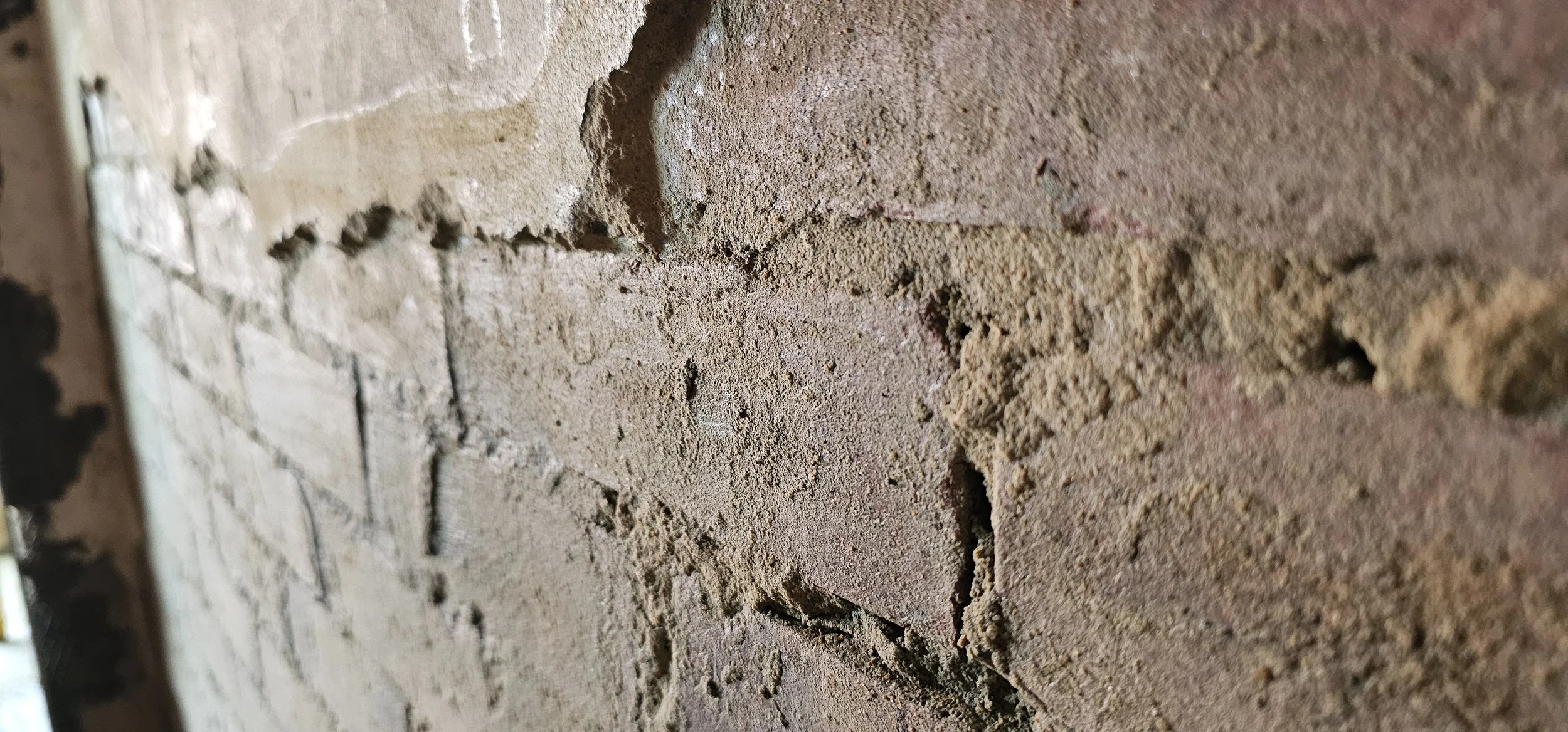 Close-up of a brick wall with blown render, textured surface in earthy tones of brown, red, and tan.
