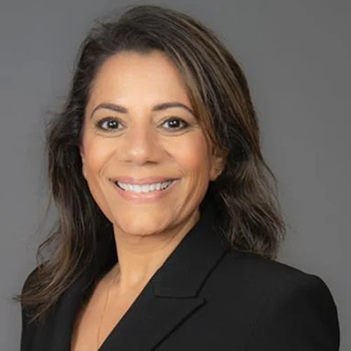 Professional woman with shoulder-length brown hair wearing a black blazer smiling against a gray background.