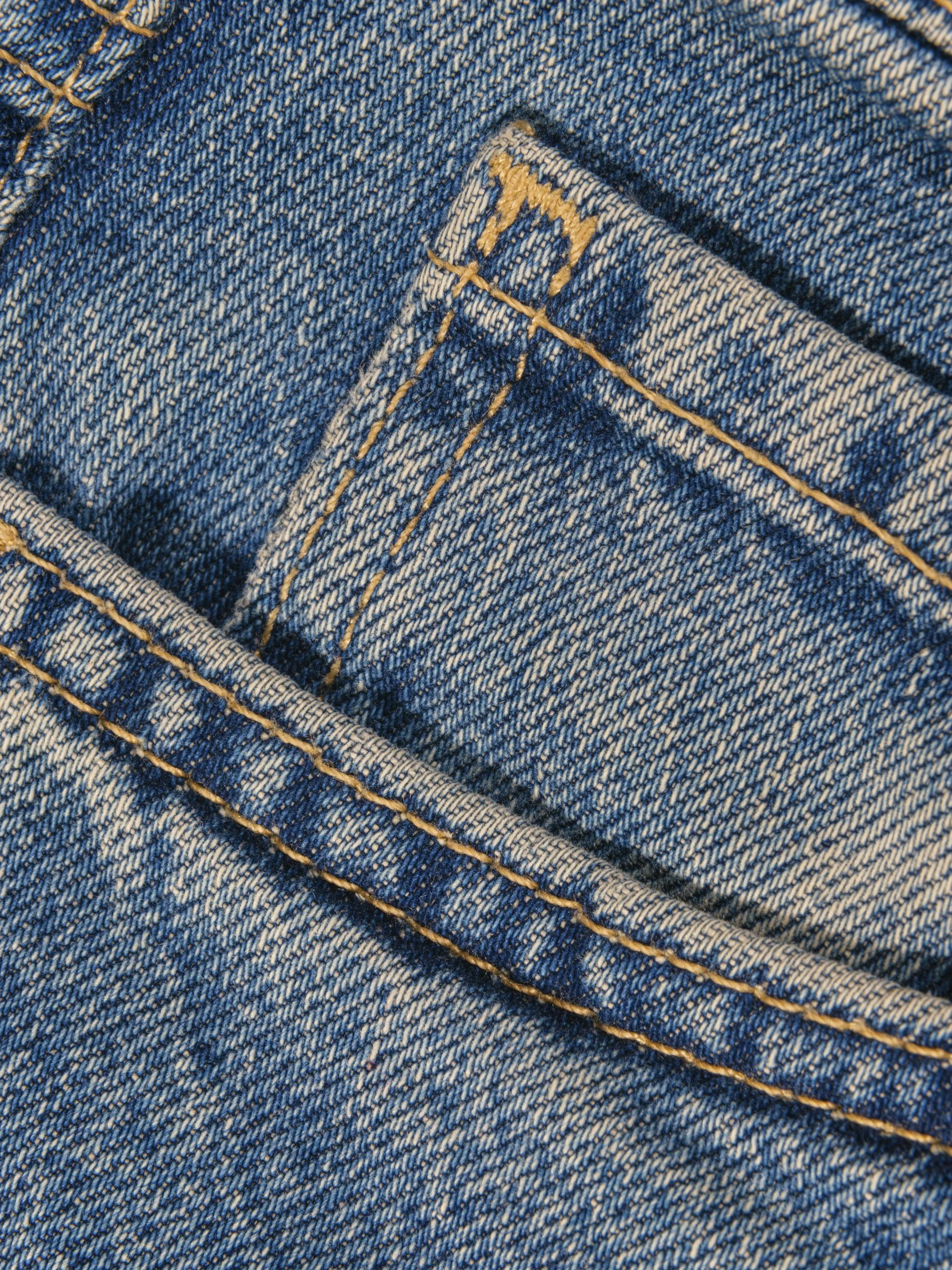 Close-up of a denim pocket with orange stitching and a small sewn label with part of a letter visible.