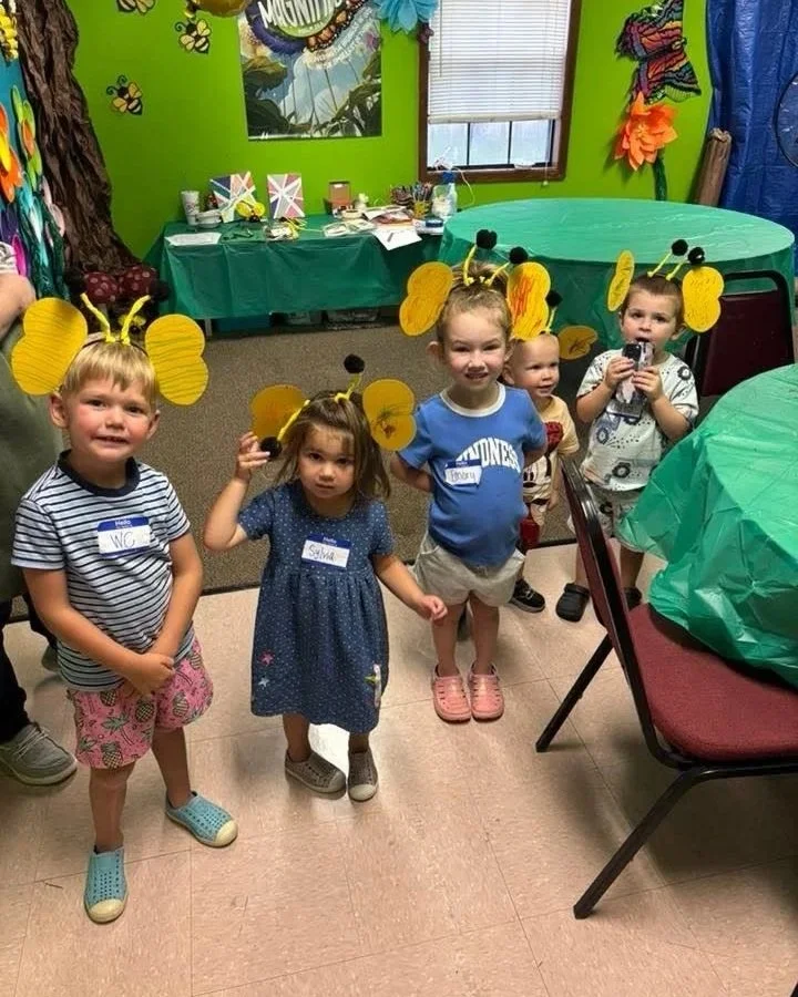 Four children dressed as bees with yellow antennae and wings in a decorated party room.