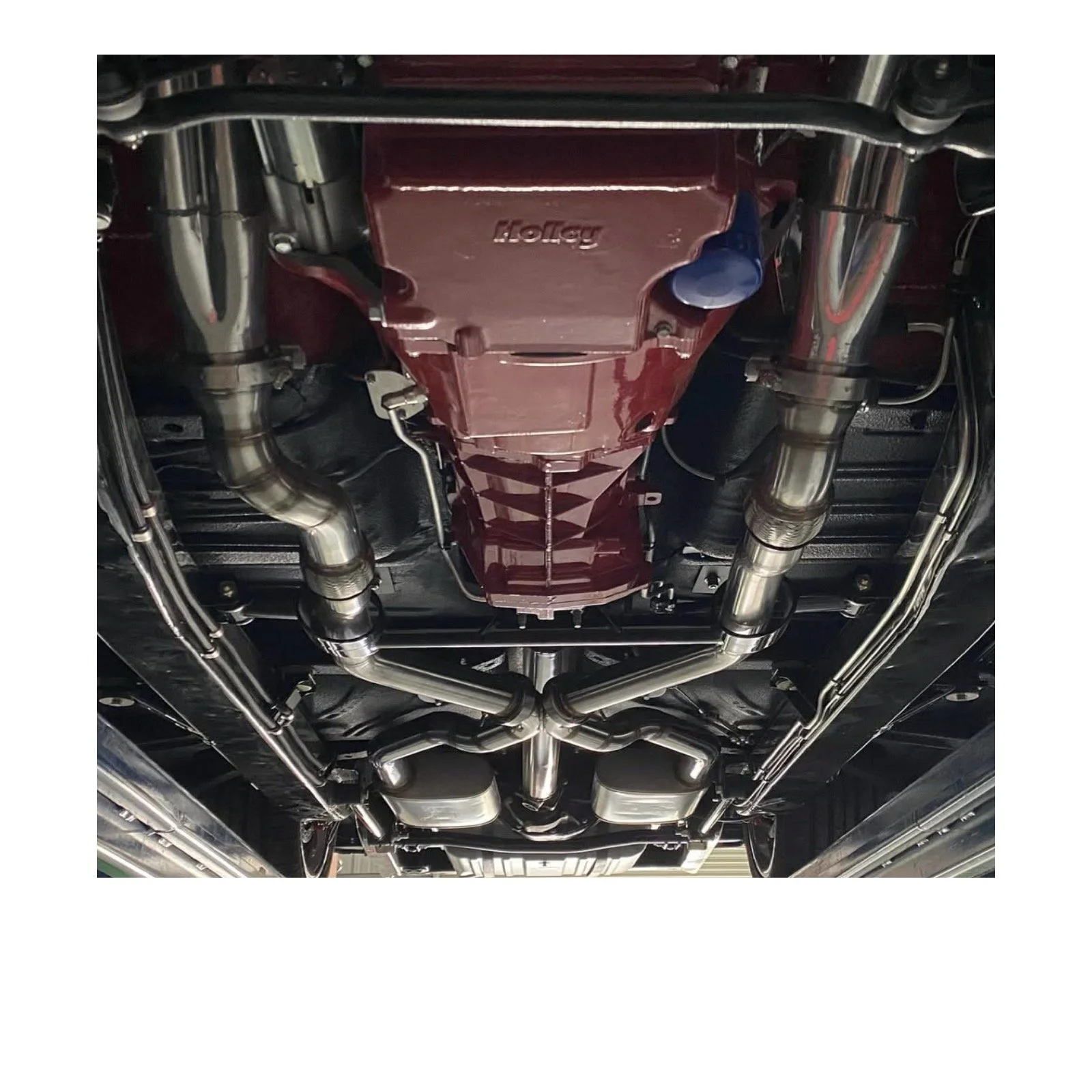 Underneath view of a car's chassis showing a red transmission, shiny exhaust pipes, and metal components.