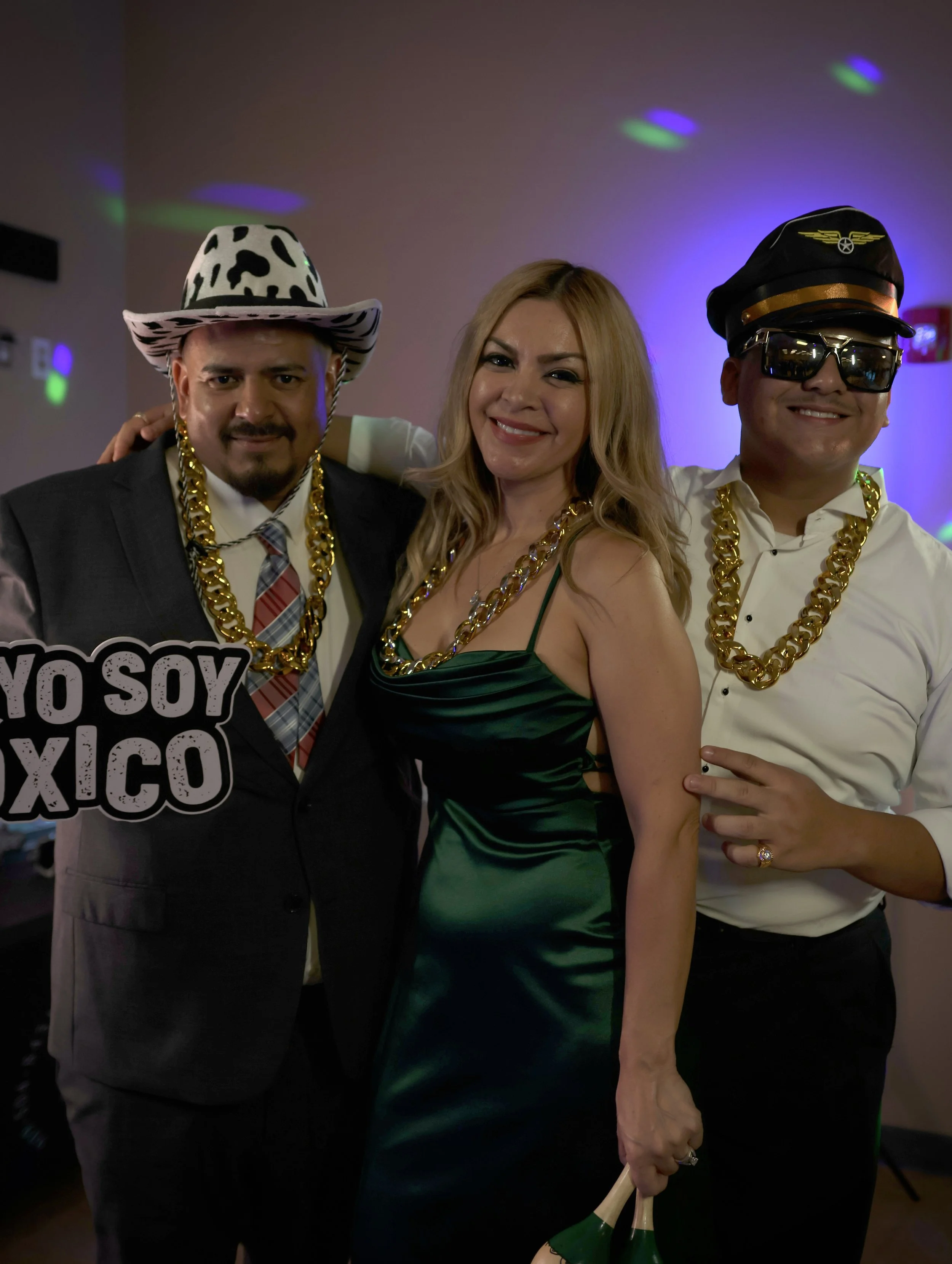 Three people celebrating at a party, wearing gold chains and costumes.
