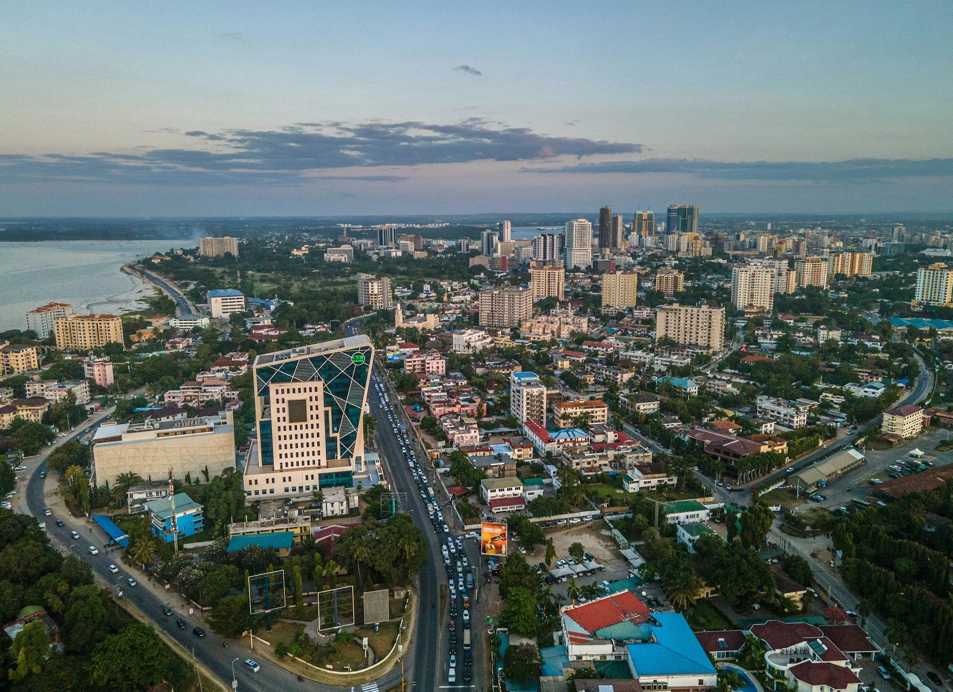 An aerial view of a city skyline near a body of water, with numerous buildings, roads, and greenery.