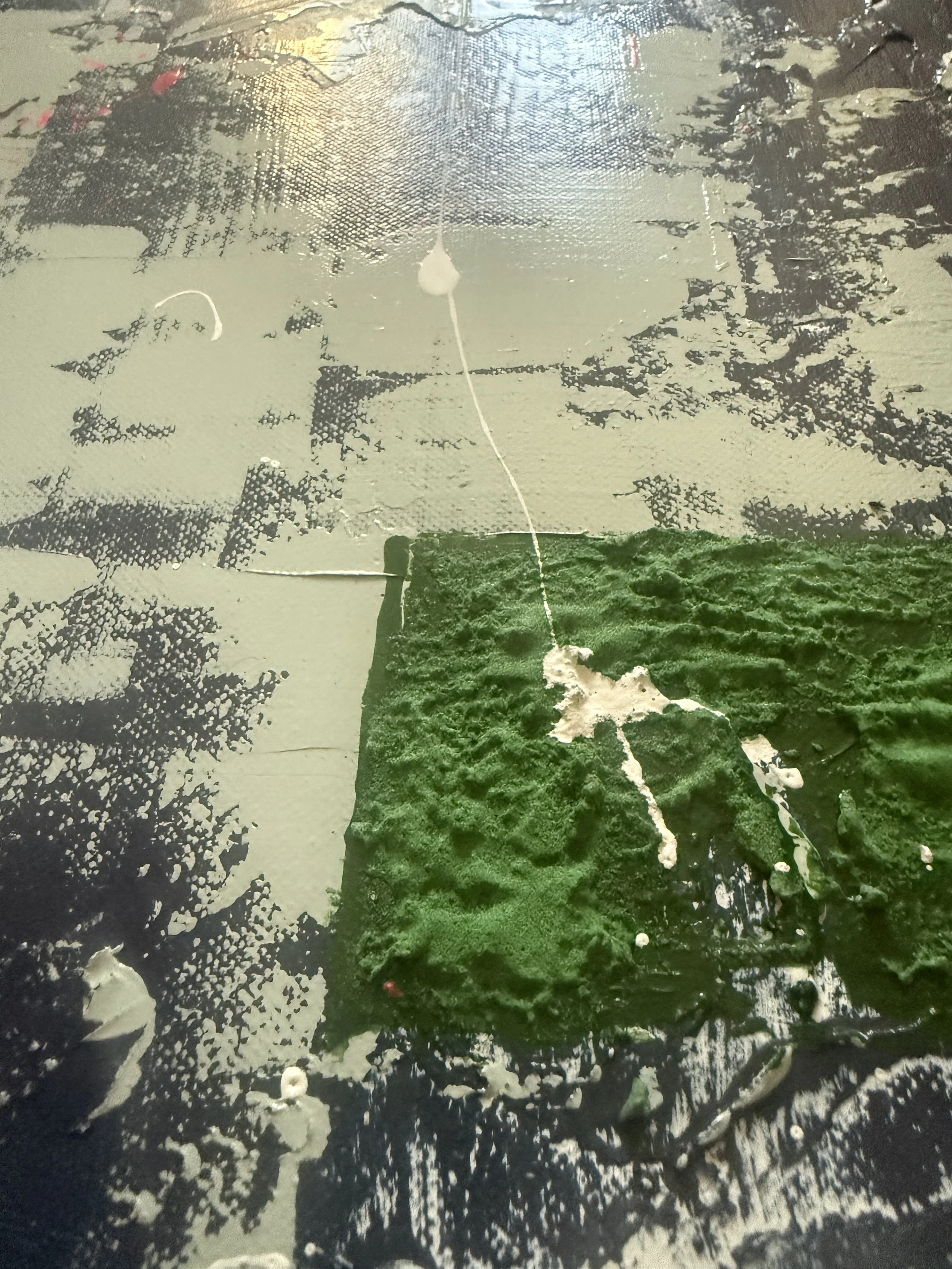 Une surface recouverte de peinture verte avec de la peinture blanche en train de couler dessus, entourée de taches de peinture noire et grise.