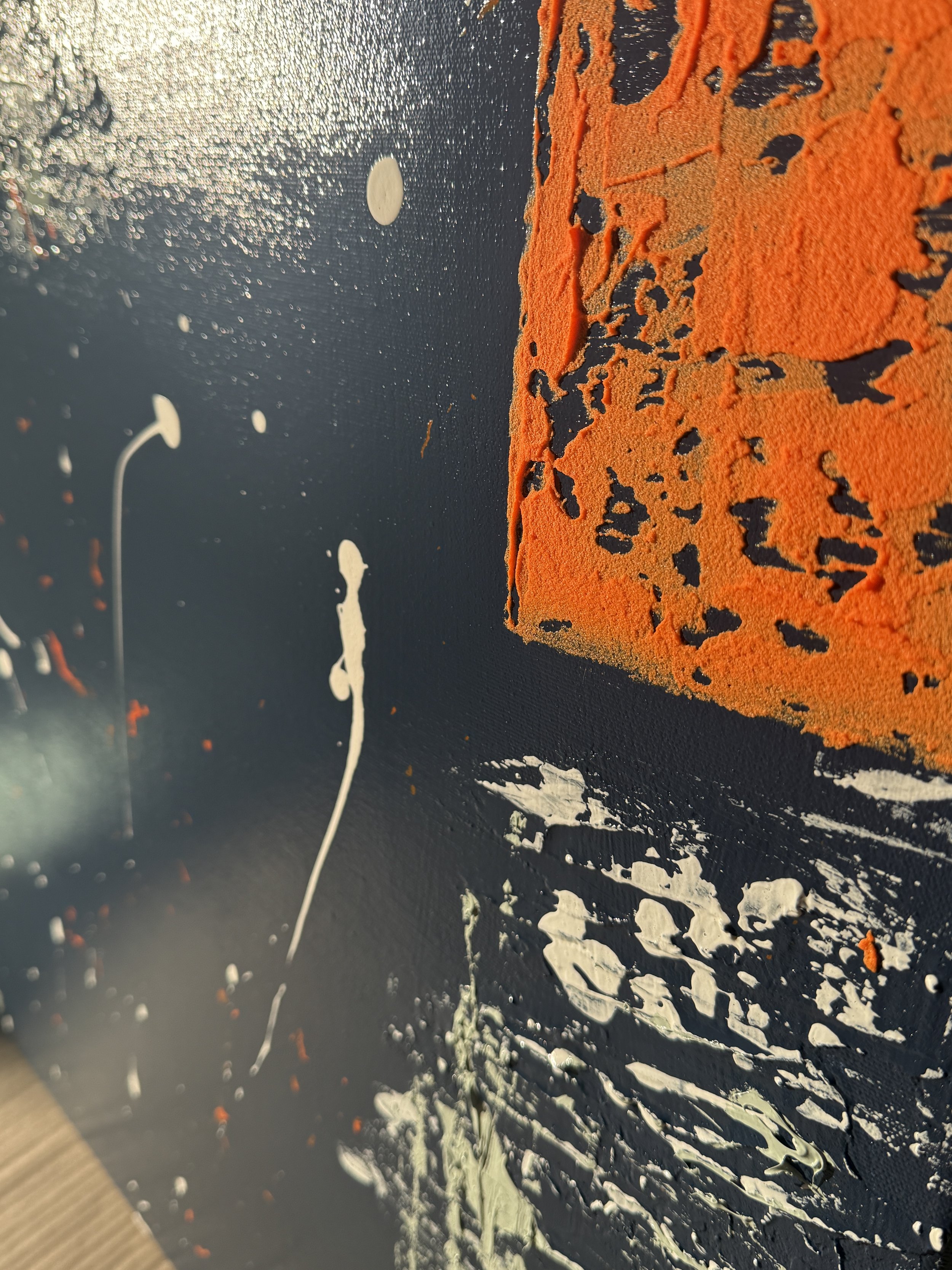 Peinture abstraite avec une grande texture orange ressemblant à un cube sur un fond noir, avec des éclaboussures de blanc et quelques touches de vert clair.