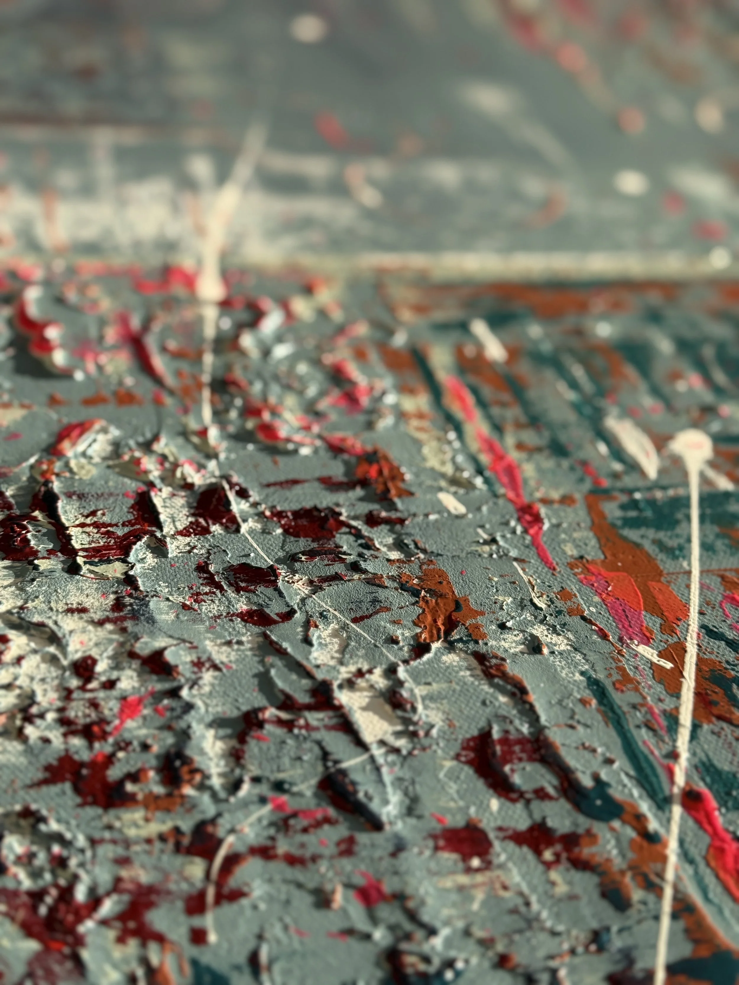 Peinture abstraite épaisse avec des taches de rouge, blanc, beige et brun sur une surface gris foncé.