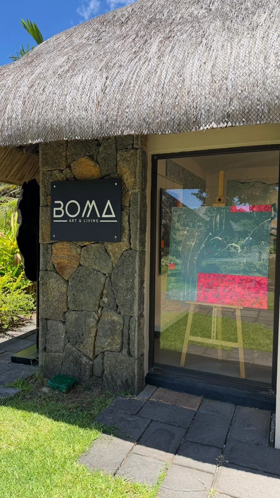 Façade d'un bâtiment en pierre avec un panneau noir indiquant 'BOMA ART & LIVING', une fenêtre en verre avec une œuvre d'art abstraite visible à l'intérieur.