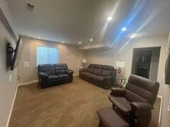 Living room with two black sofas, a leather recliner, and a wall-mounted TV in a well-lit space.