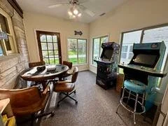 A dining area with a round wooden table, six chairs, large windows, and an indoor grill.