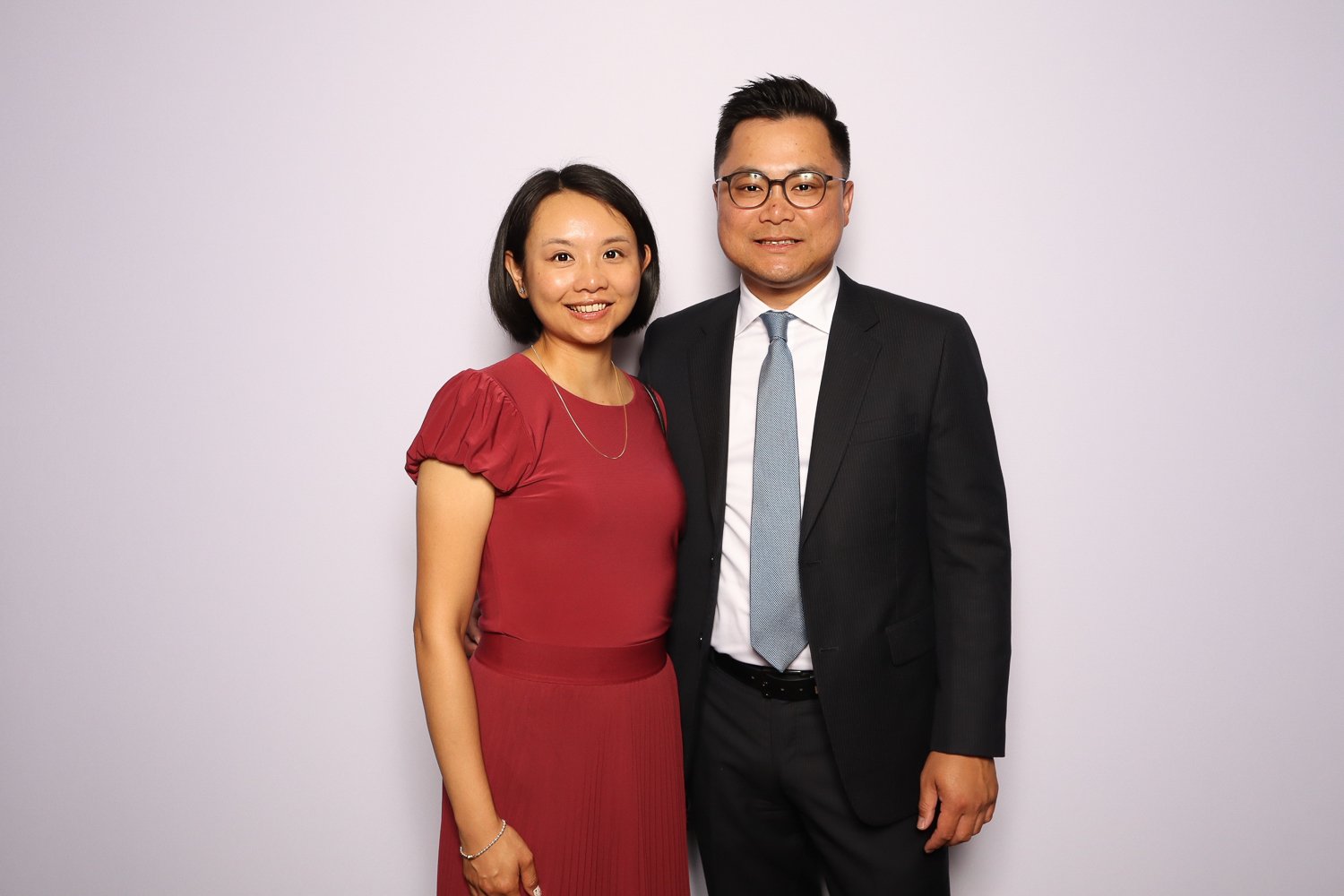 A man and woman standing side by side, smiling, dressed in formal attire, against a plain background.