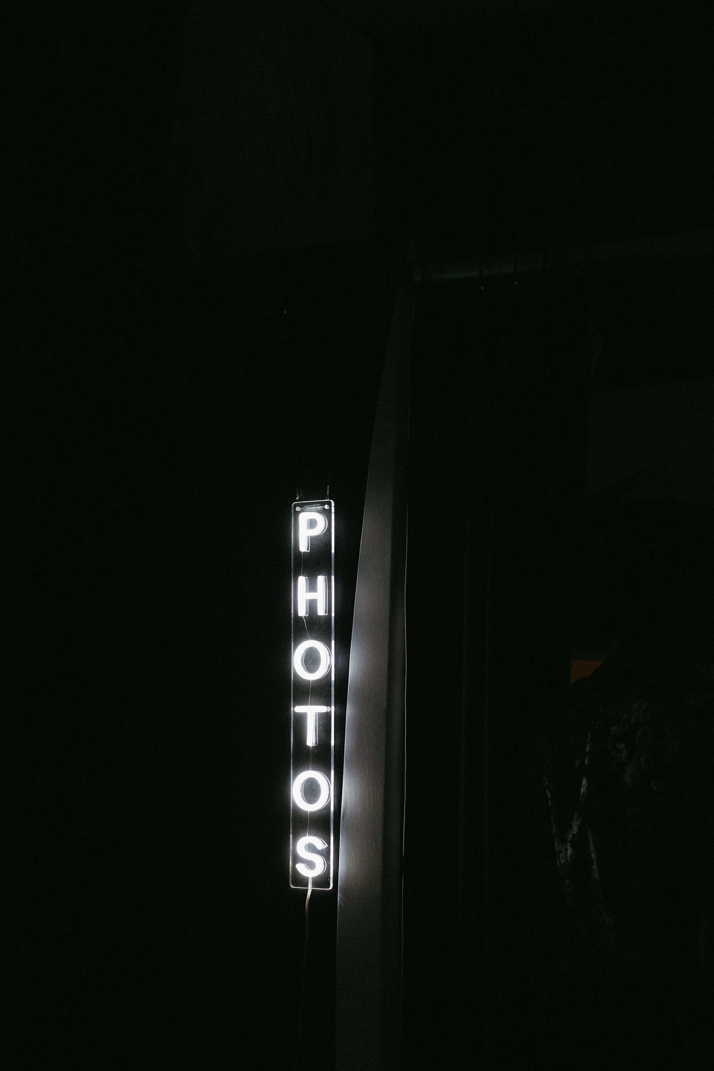Illuminated vertical sign spelling 'PHOTOS' in a dark room.