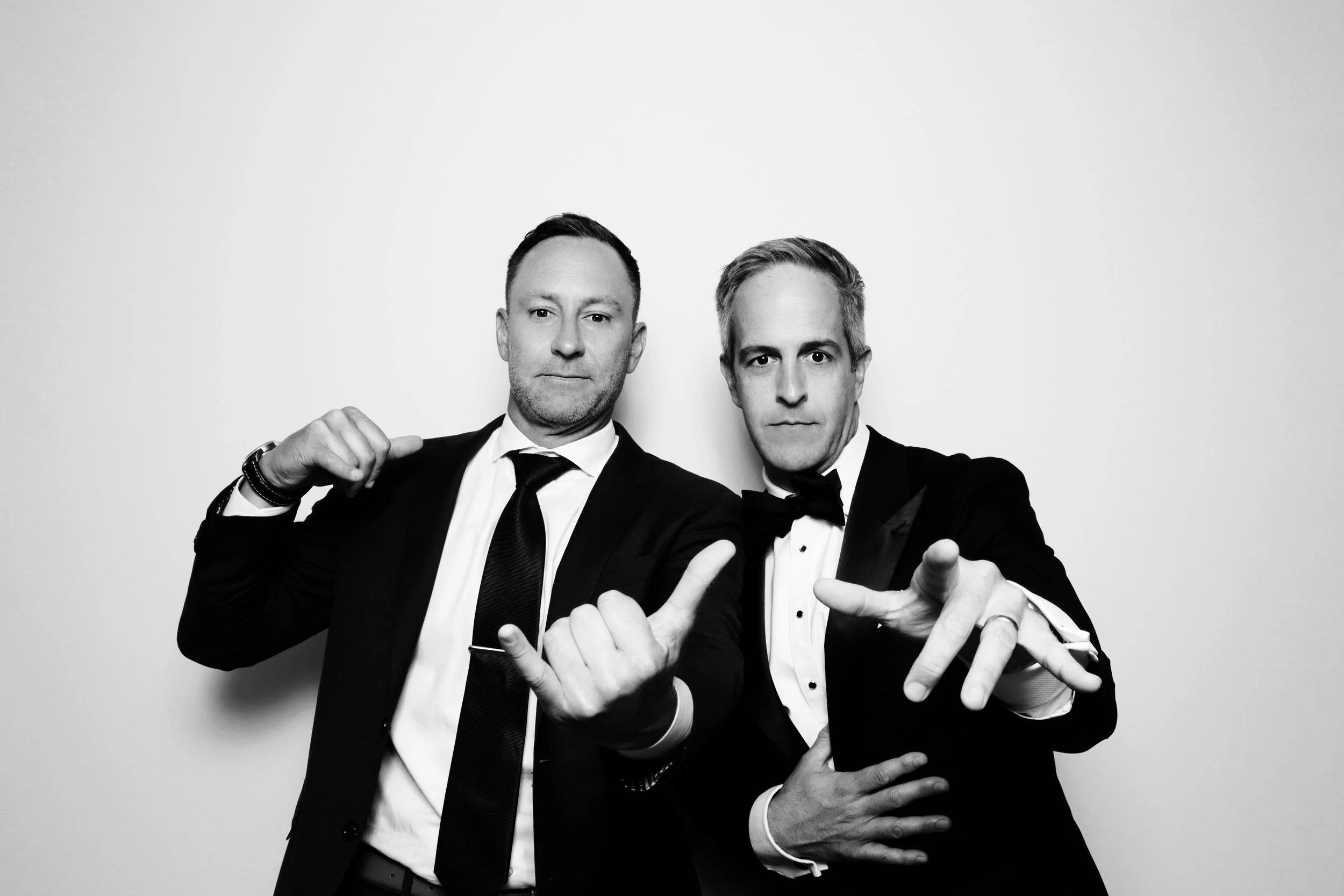 Two men in tuxedos posing confidently against a plain white background.