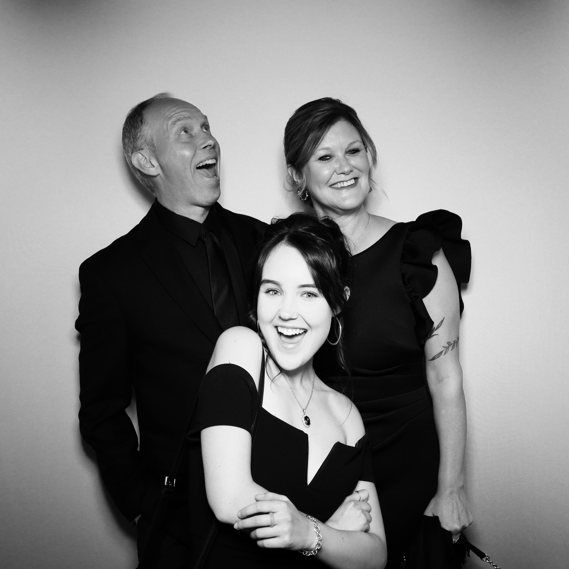 Black and white photo of three people smiling and posing together, with a plain background.