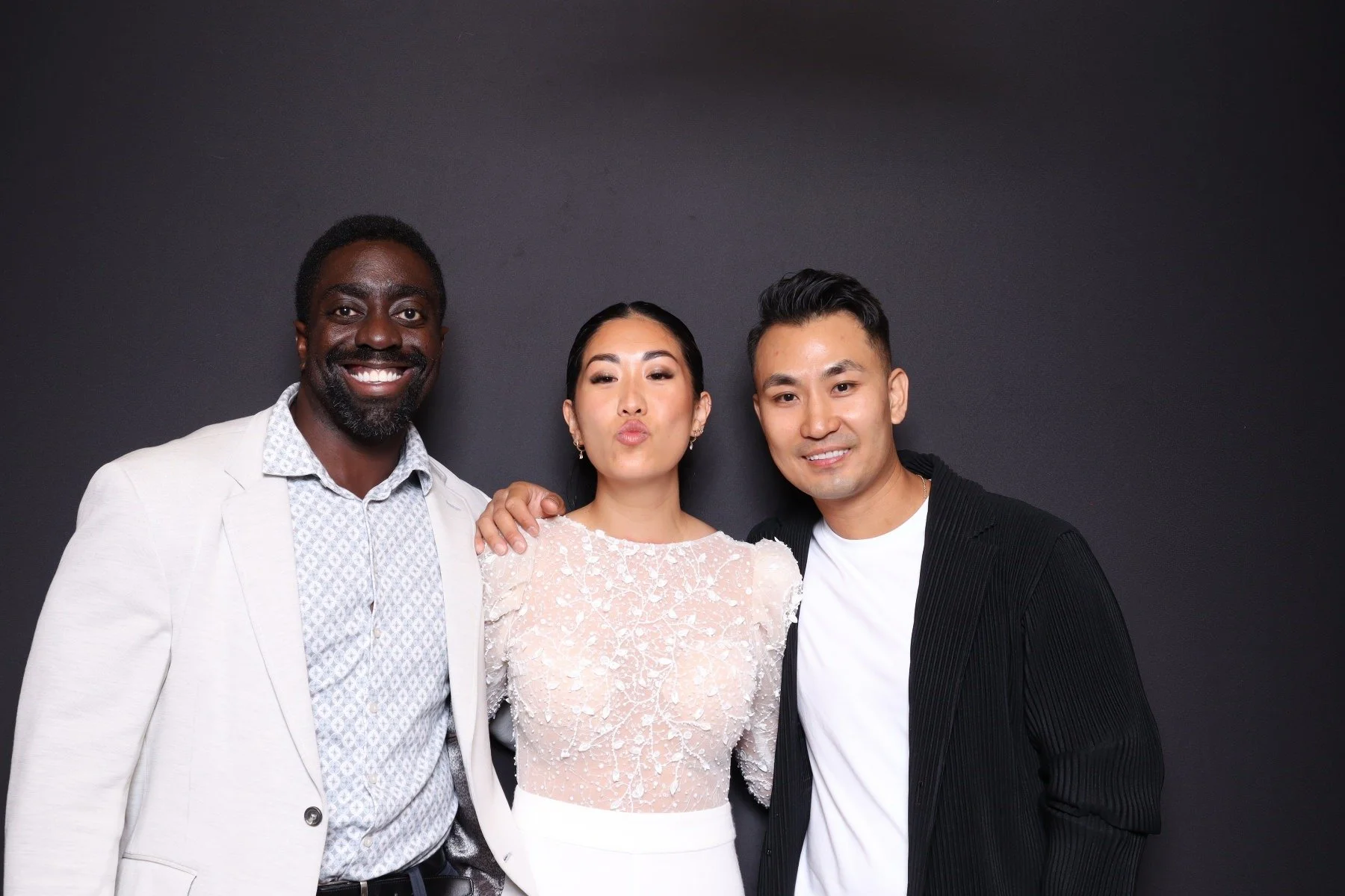Three friends posing together against a black background, smiling, with the woman making a kissy face in the middle.