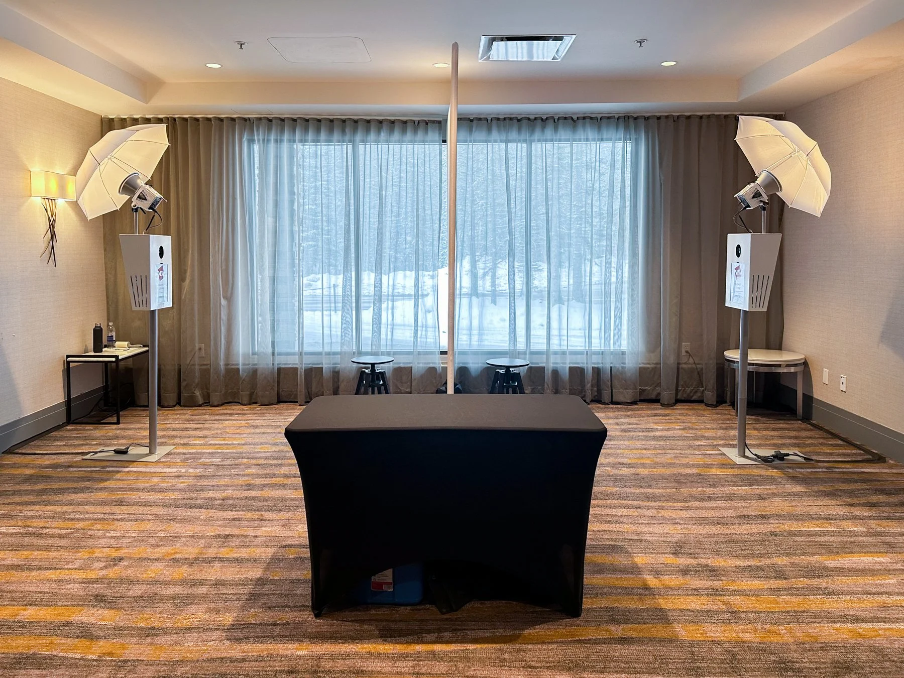 Empty conference room with two photography umbrellas on light stands, a black table, and a large window with snow outside.