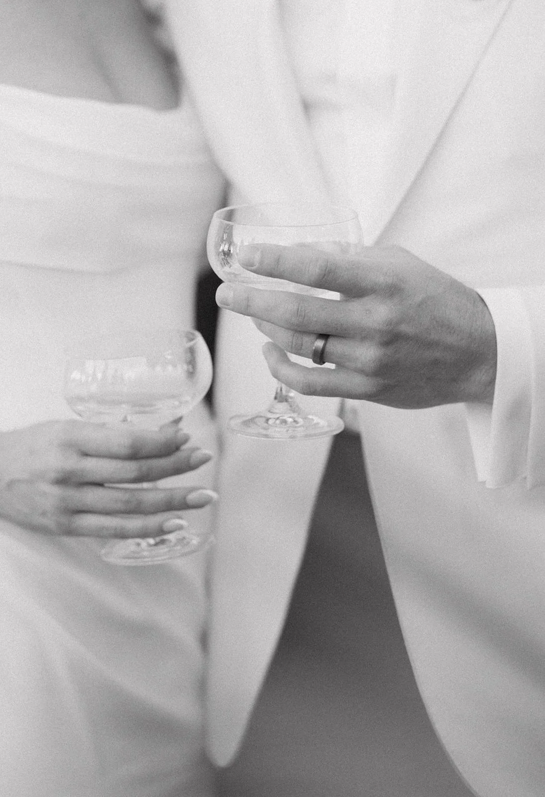 Close-up of two people holding empty glasses, possibly at a celebration or event, dressed in formal attire.