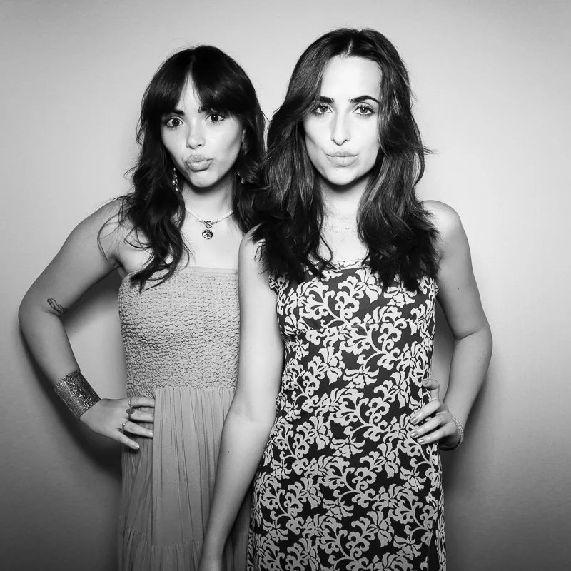 Two young women standing close together, both making a pouty face and looking at the camera, in a black and white photo against a plain background.