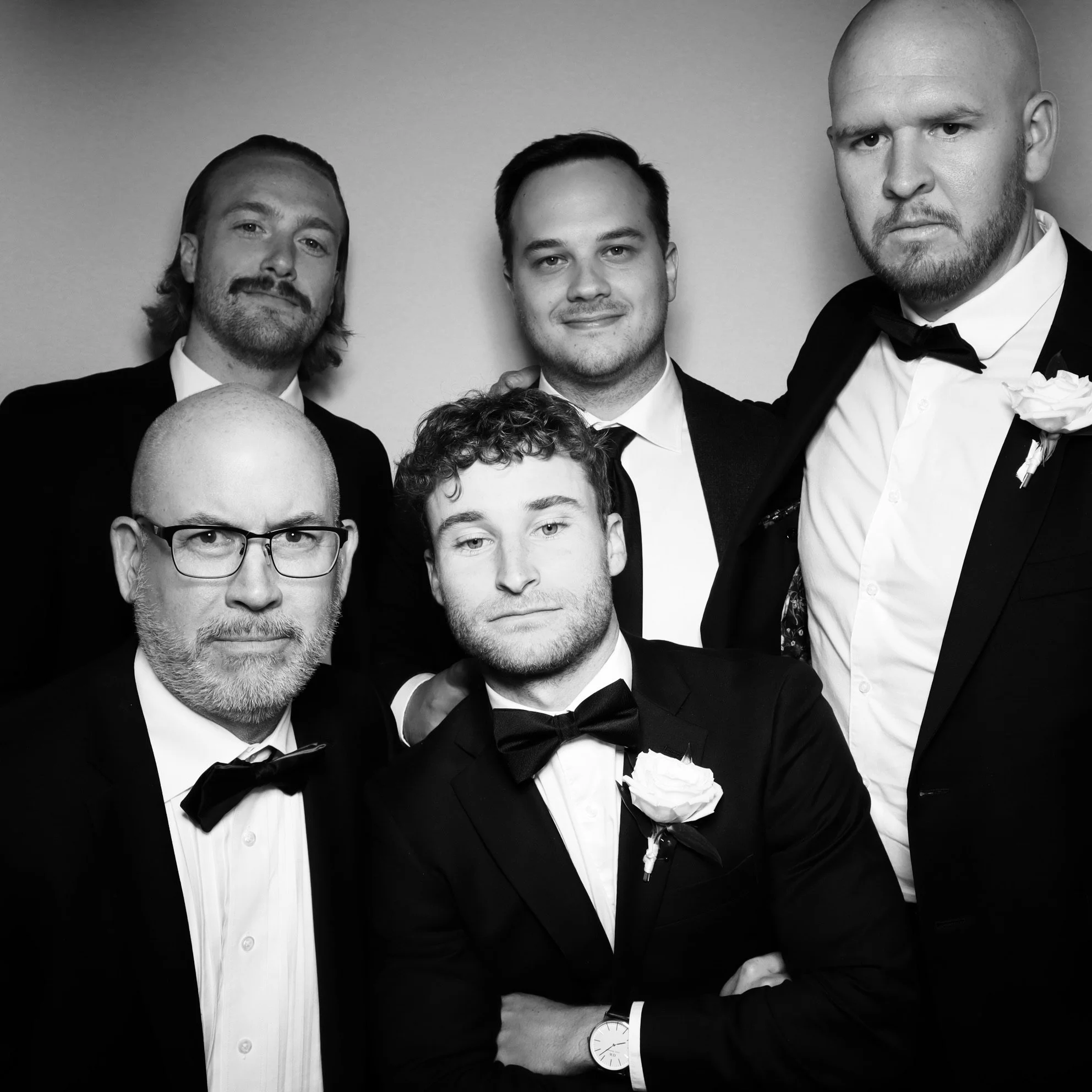 Group of six men in tuxedos at formal event, some wearing bow ties, posing for a black-and-white photograph.