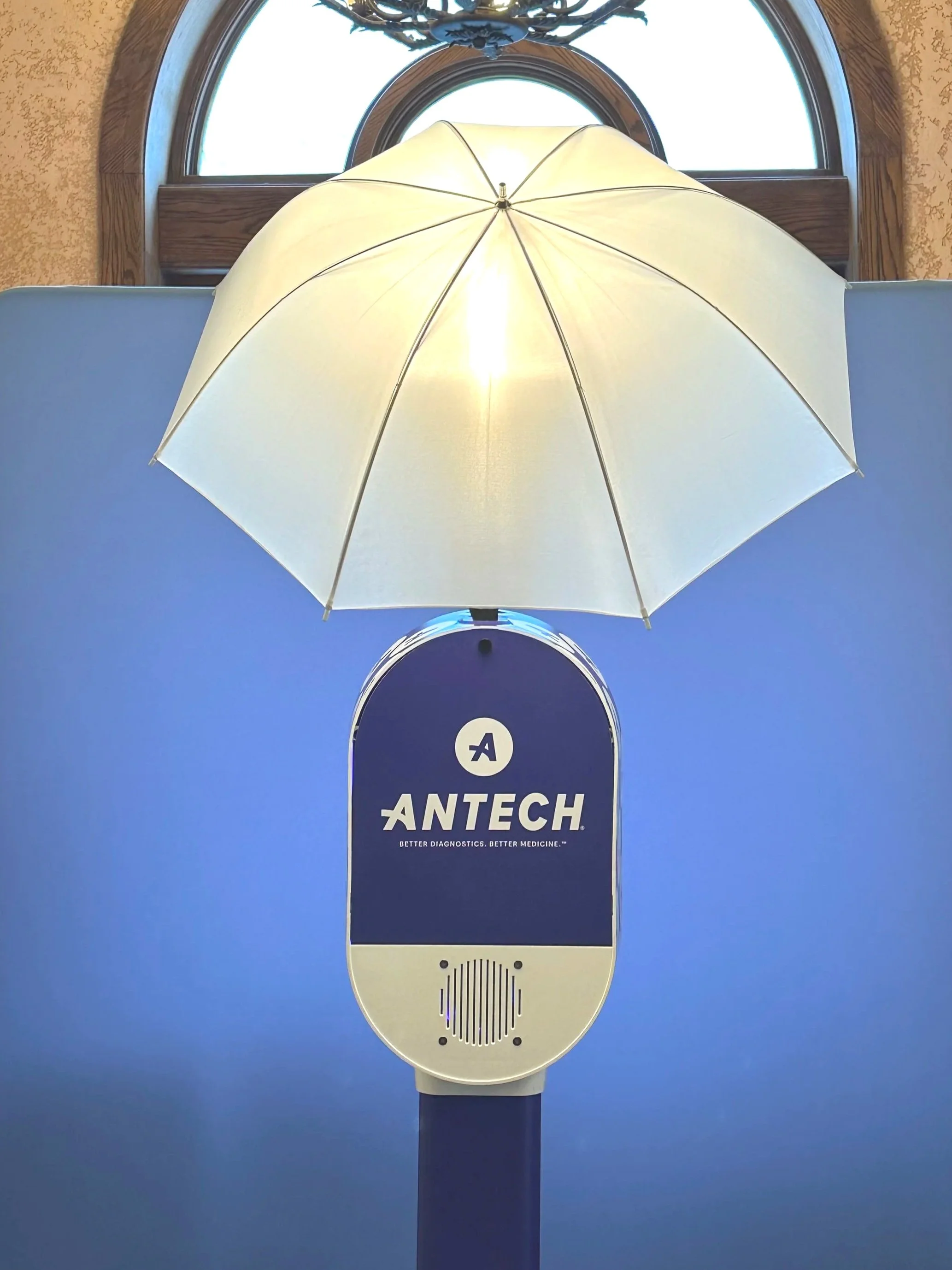 An super bright white umbrella mounted above a device labeled "Antech" with the tagline "Better diagnostics. Better medicine." The device has a circular speaker grill at the bottom and a blue background.