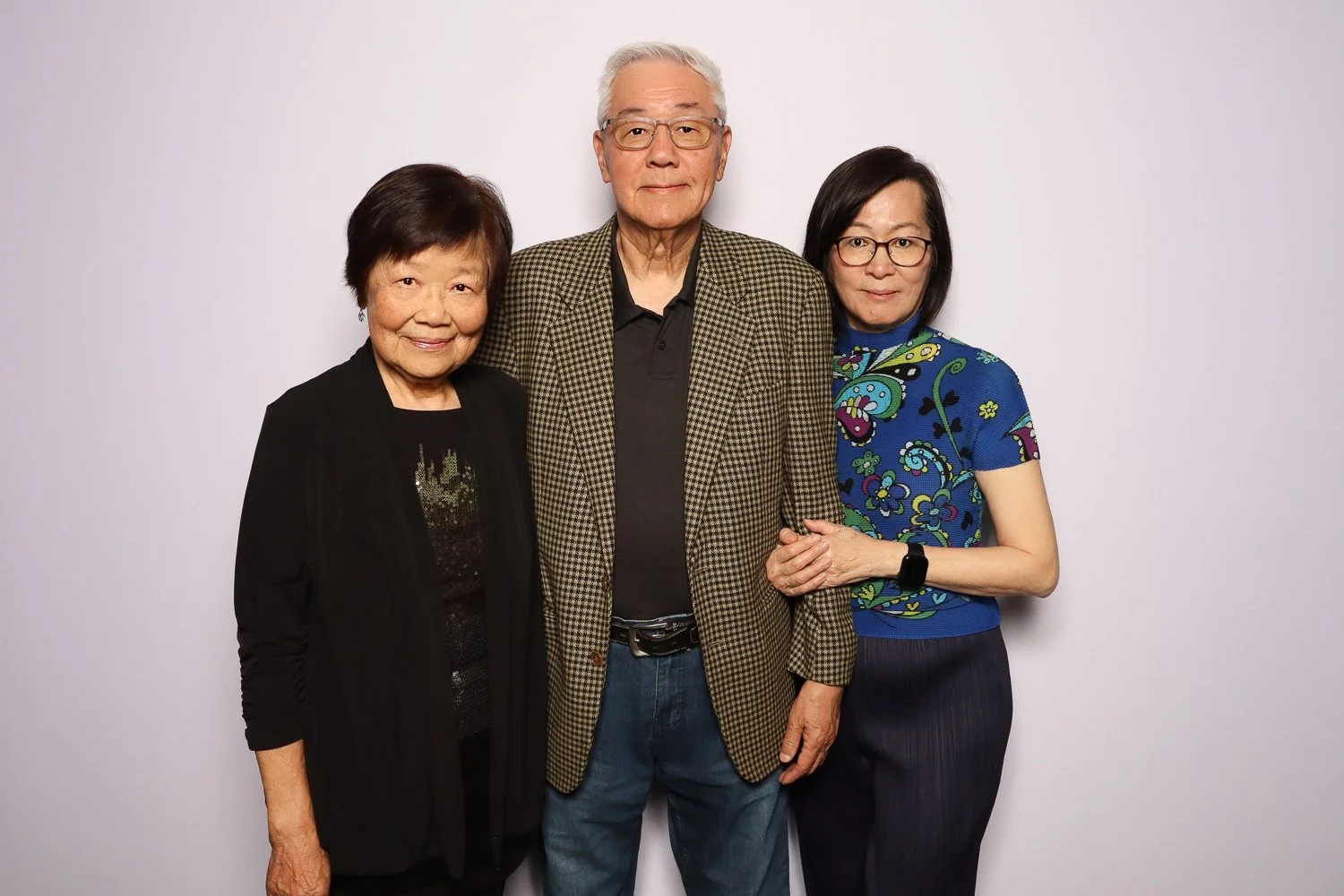 Three Asian adults, two women and one man, standing close together against a plain white background, smiling at the camera.