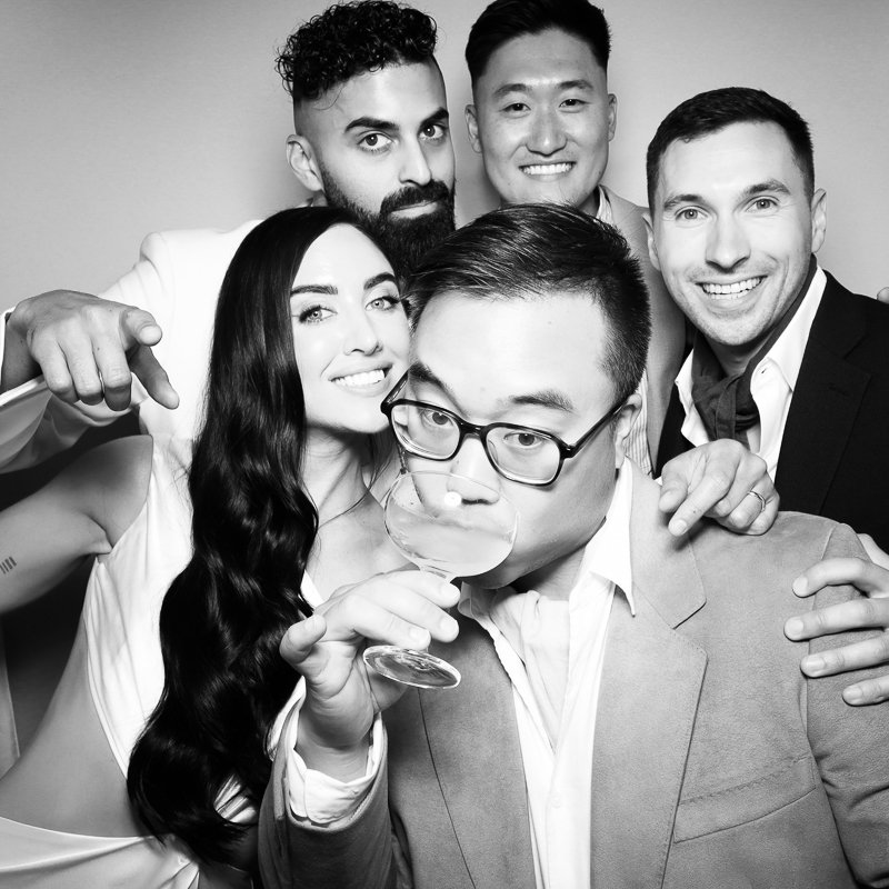 Group of six friends taking a selfie, with one person drinking from a large cocktail glass, in black and white.