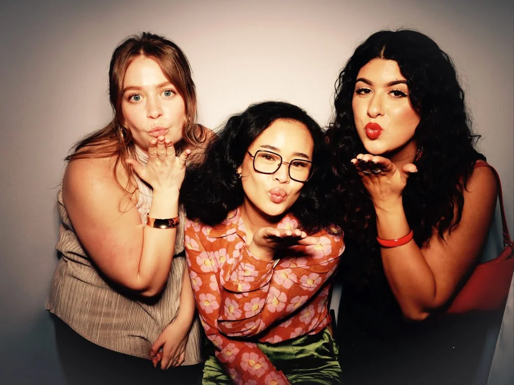 Three women blowing kisses at the camera against a plain background.