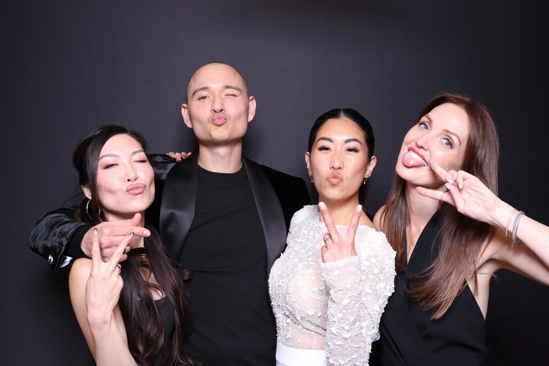 Four friends posing playfully against a black background, making funny faces and gestures.