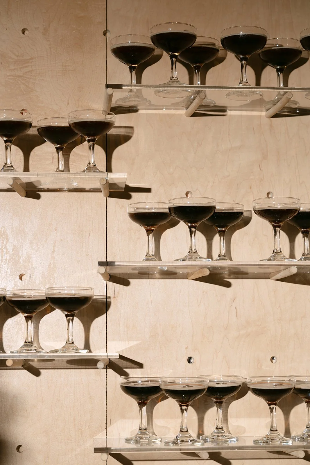 Multiple glasses of red wine served on wooden shelves against a light wooden wall.