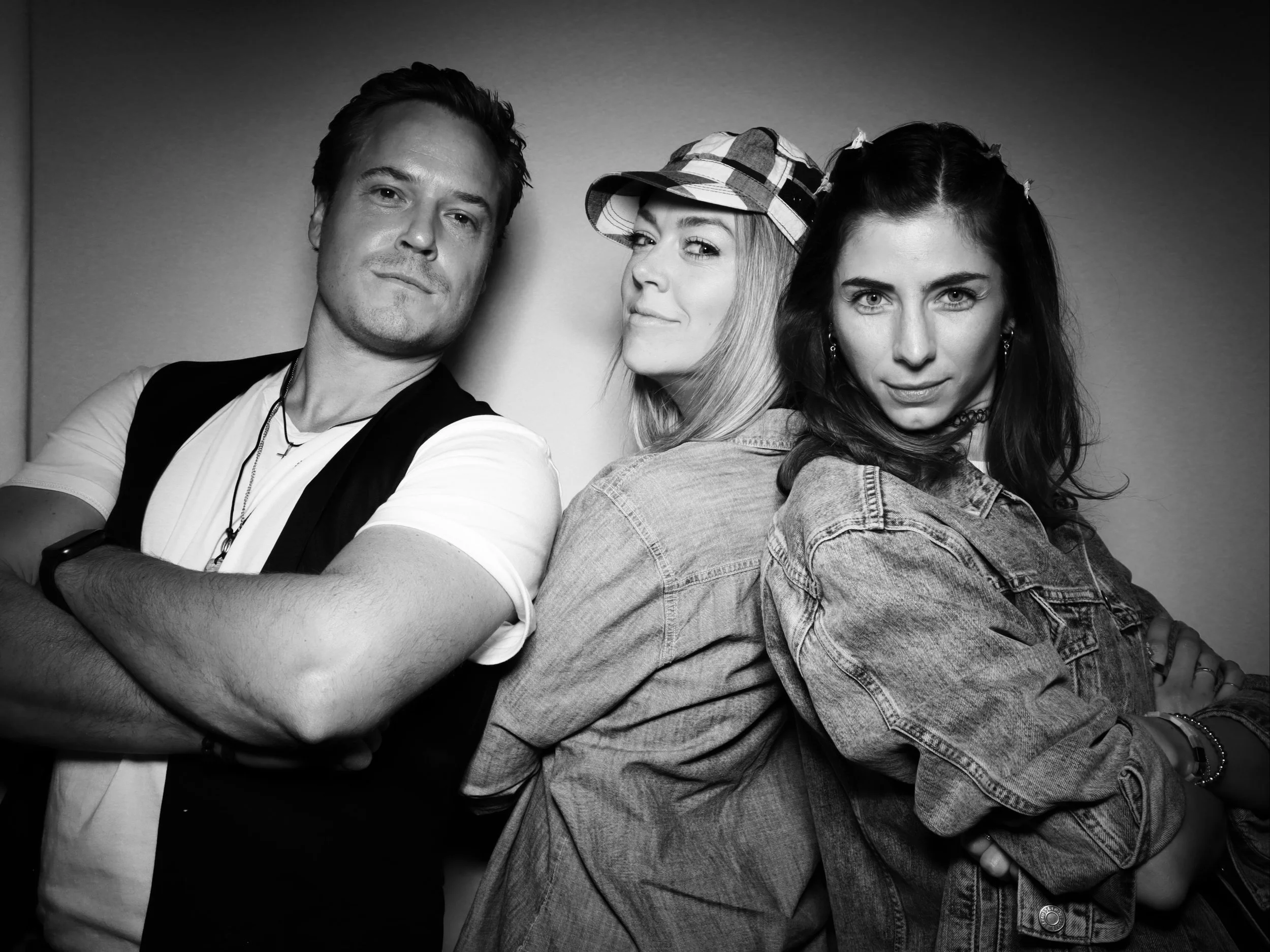Three young adults, two women and a man, posing together in black-and-white, with serious expressions and arms crossed.