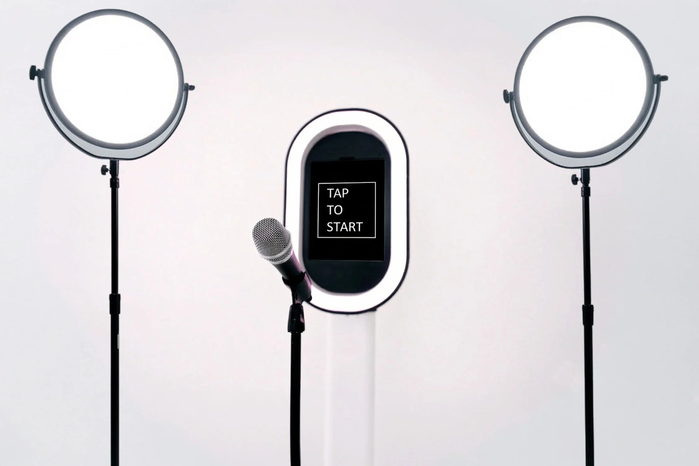 A photography studio setup with two studio lights on stands, a microphone, and a digital screen that says 'TAP TO START' on a white background.