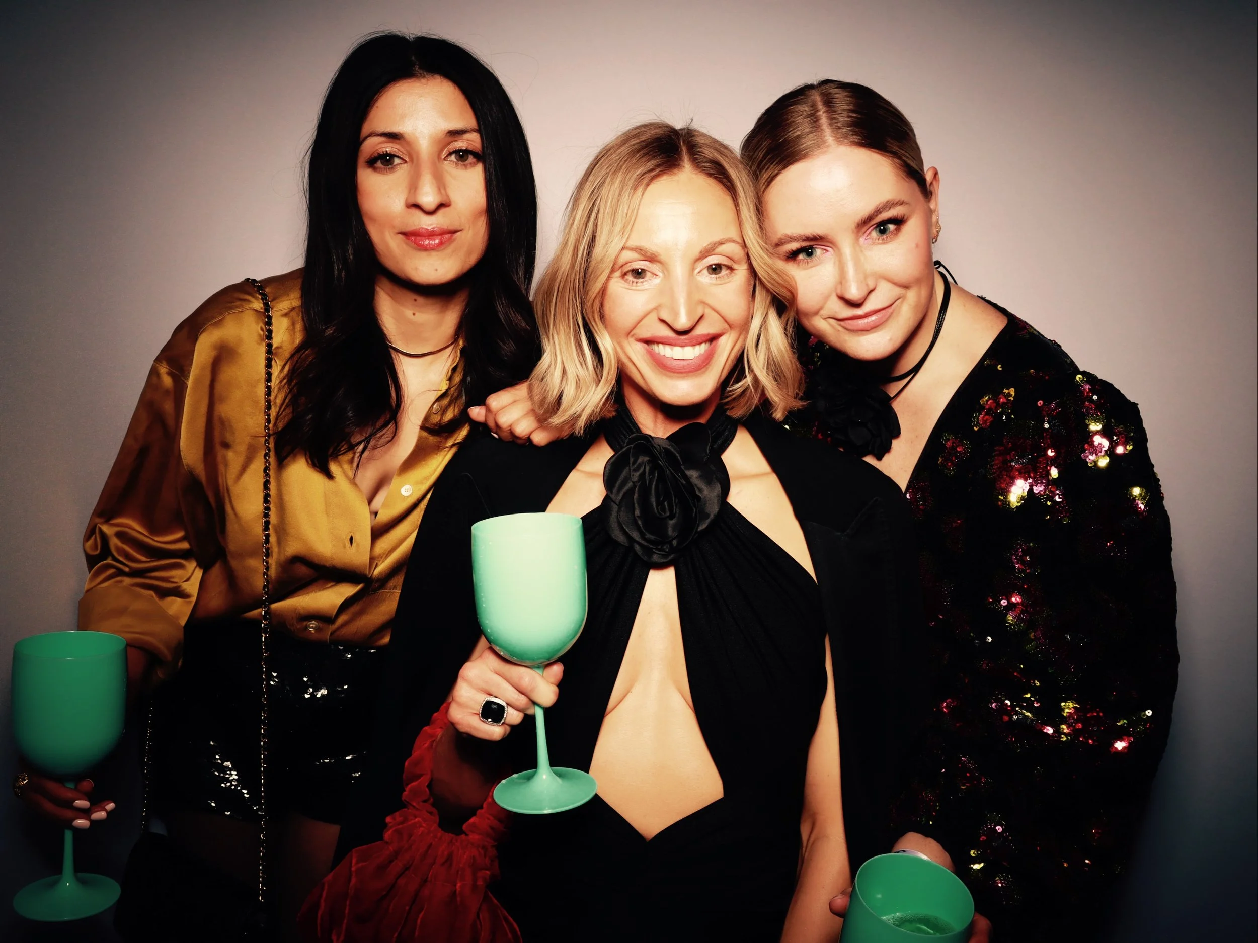 Four women smiling and holding green cups at a celebration or party.