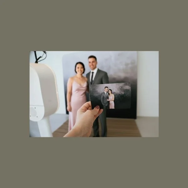 Person holding a photograph of a couple in front of a larger poster of the same couple at an art exhibit or gallery.