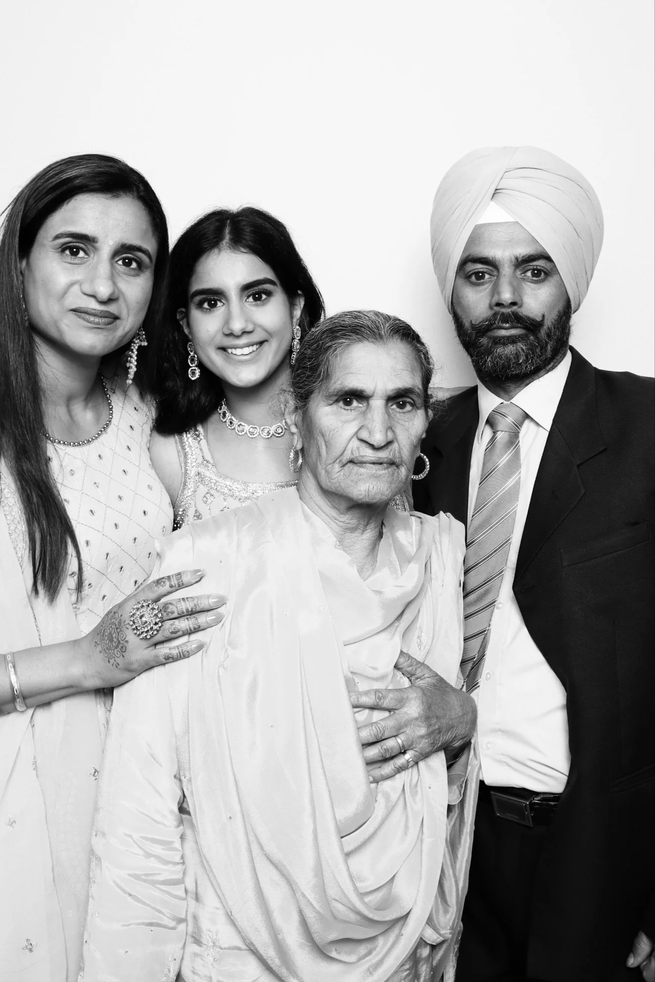 A black and white photo of five people standing together against a plain background, including two women and three men of South Asian descent, dressed in formal and traditional attire.