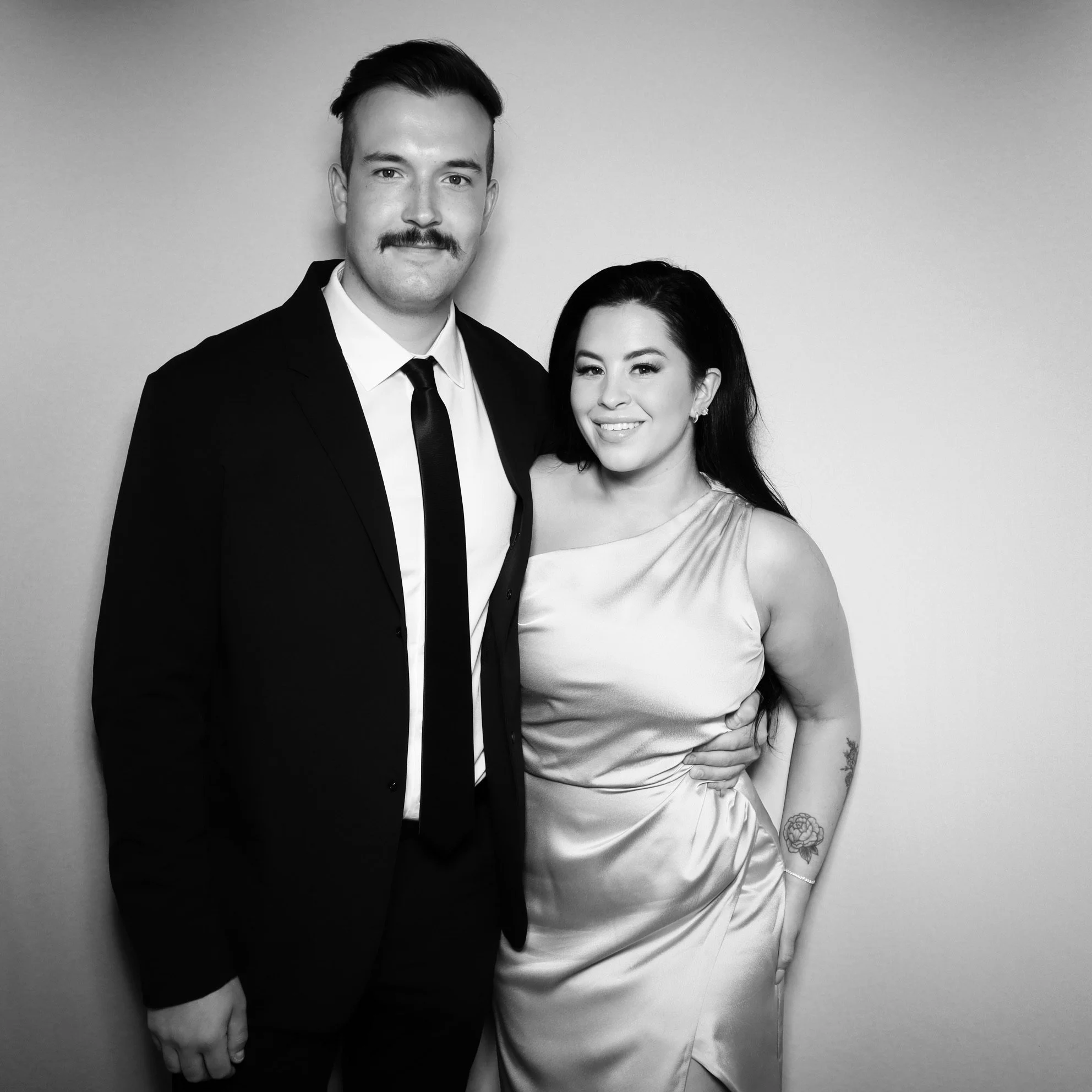 Black-and-white photo of a man in a suit and a woman in a dress, standing close together and smiling at the camera.