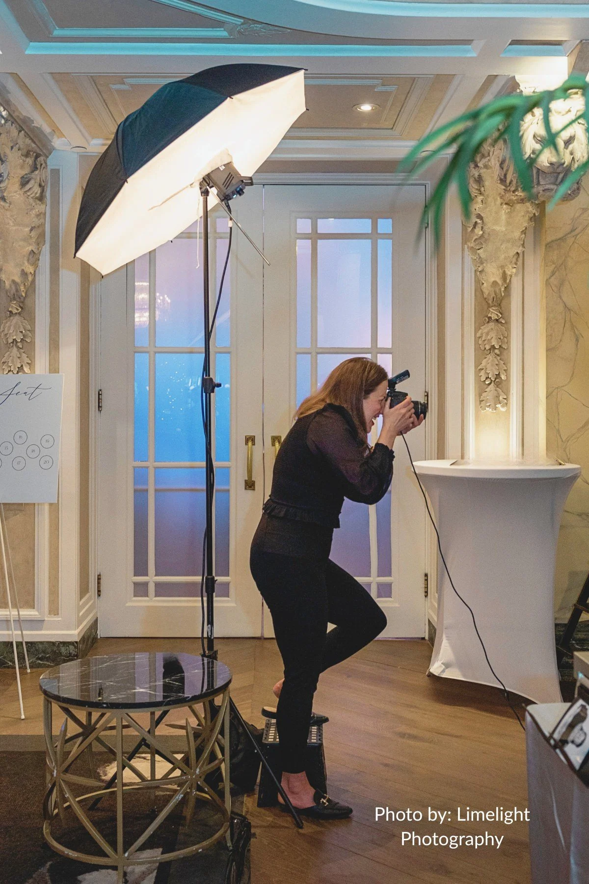 A photographer smiling while capturing guests at a live studio photographer booth rental setup featuring a professiona light, positioned in an elegant event venue.