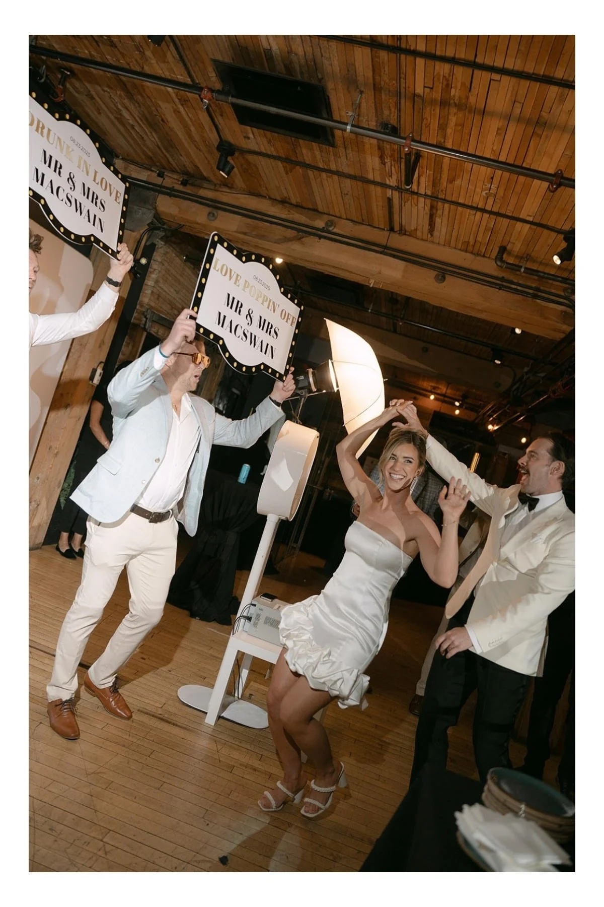A bride in a short white wedding dress and a groom in tuxedo with a white jacket enter their reception in at Charbar in the historic Simmons building in Calgary, AB
