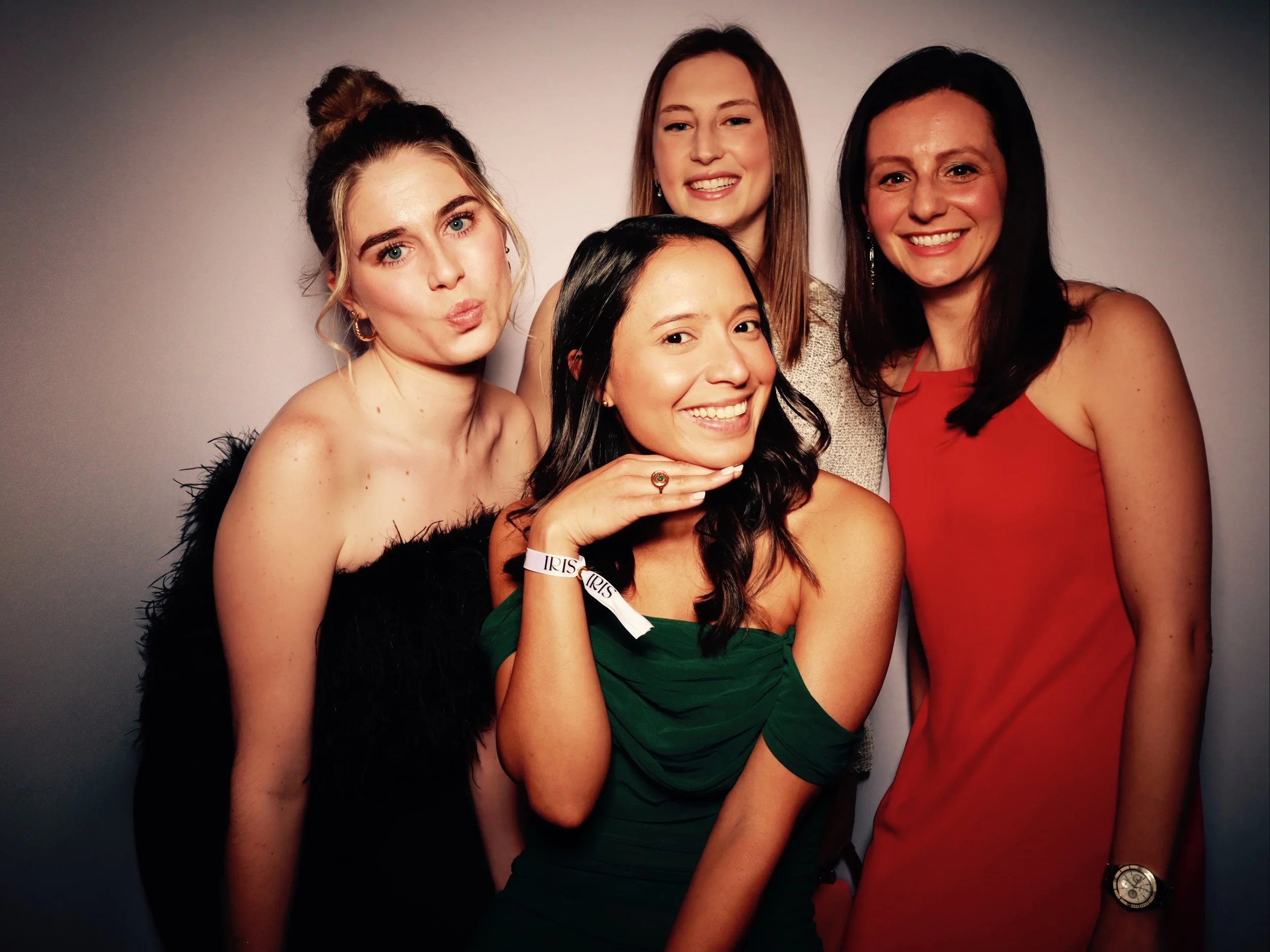 Five women posing together against a neutral background, smiling and making expressive faces, dressed in stylish dresses.