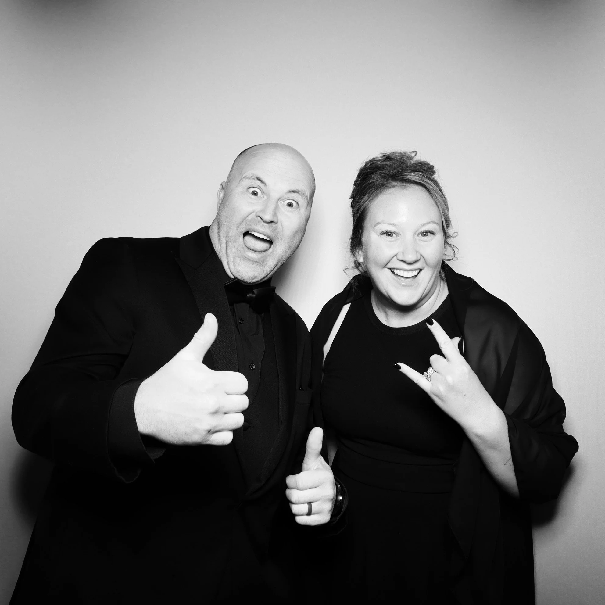 Two people dressed in black, smiling, and making enthusiastic gestures in a black-and-white photo.