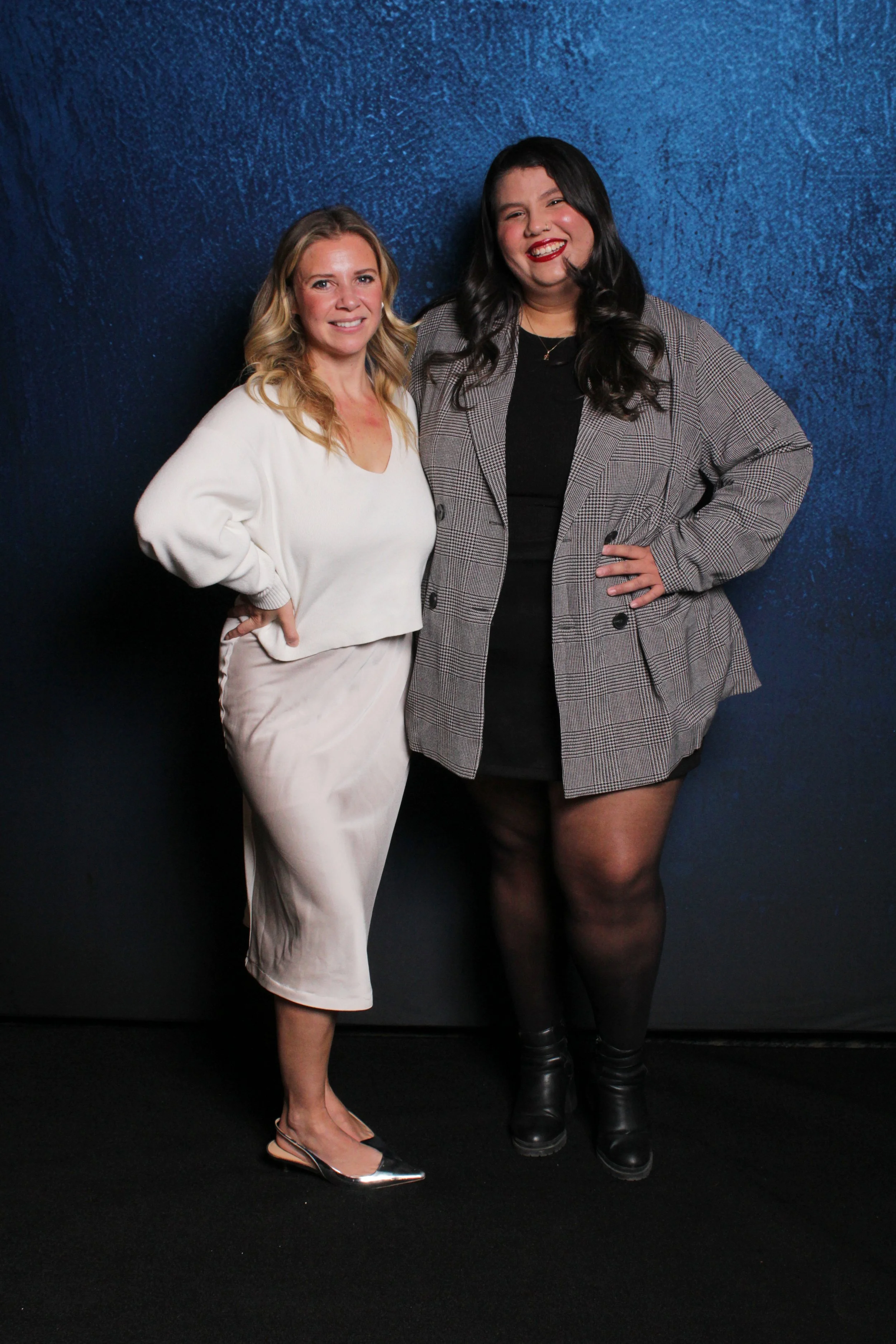 Two women standing against a blue textured wall, smiling at the camera.