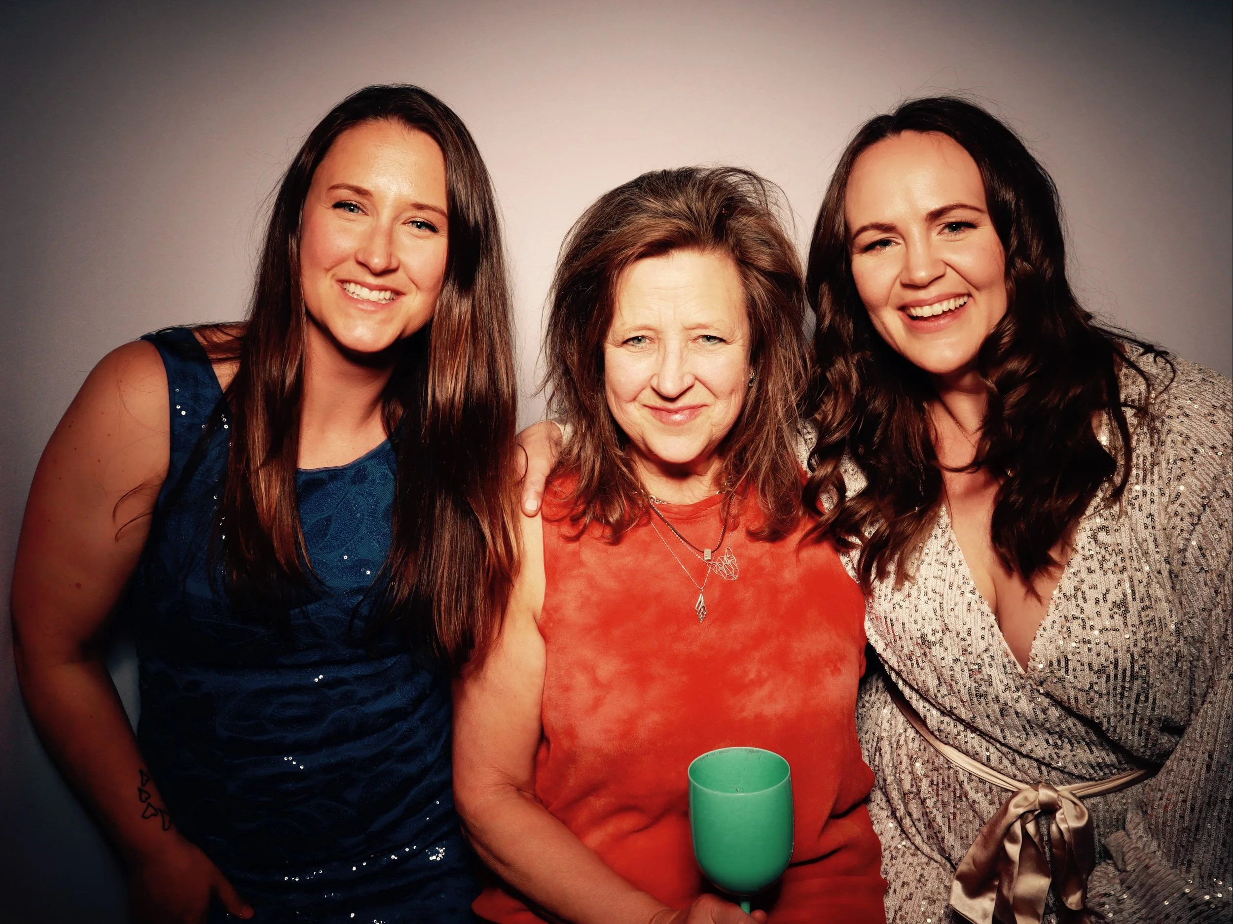 Three women smiling for a photo, the woman in the middle holding a green cup.